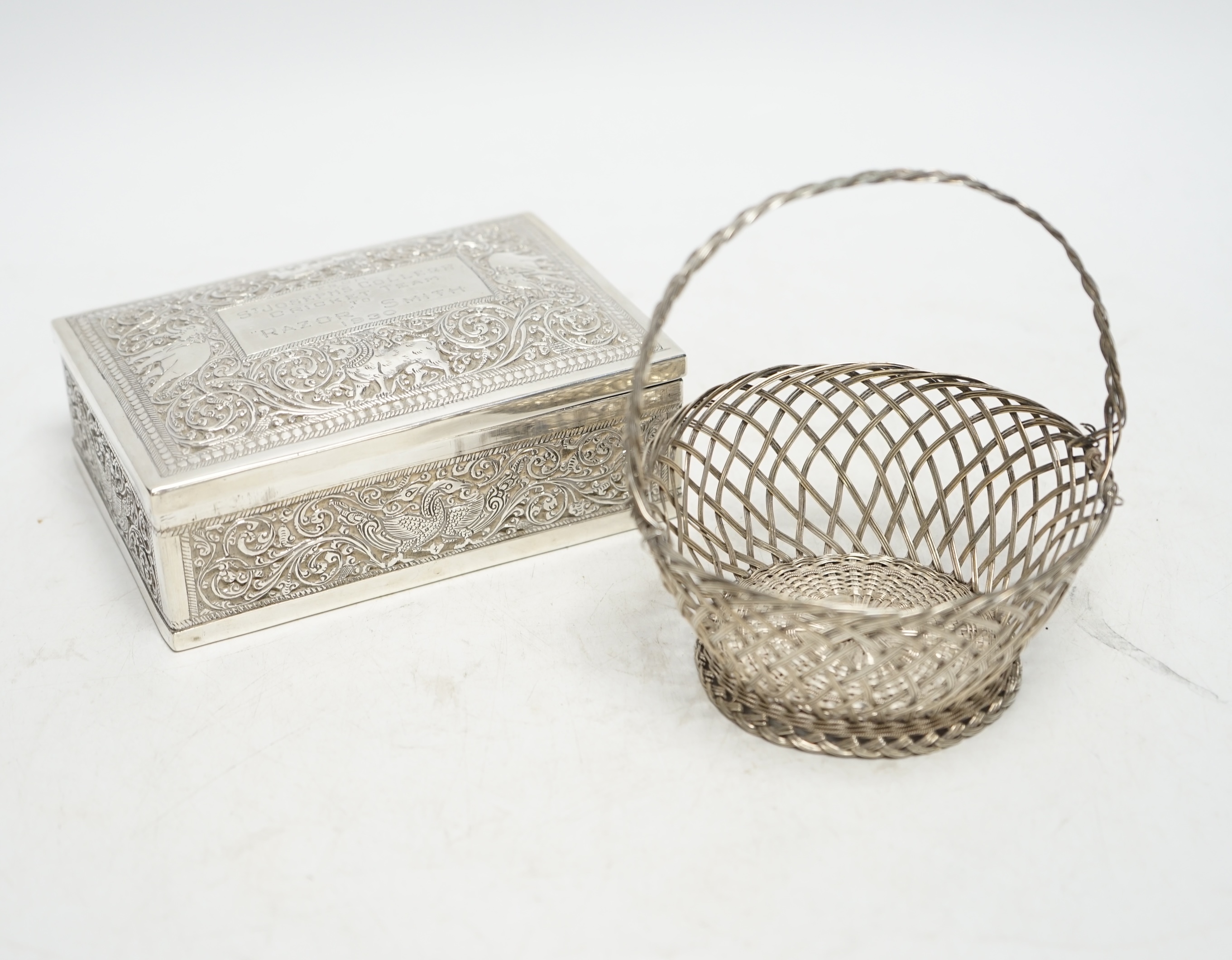 An Indian white metal mounted rectangular cigarette box, with engraved inscription, 'From St. Joseph's College Cricket Team, to 'Razor' Smith, 1930', 12.9cm, together with a white metal open work basket. Condition - fair